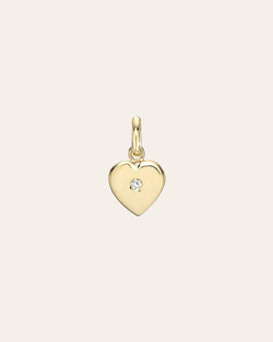 Gold heart-shaped pendant with a diamond on a light beige background