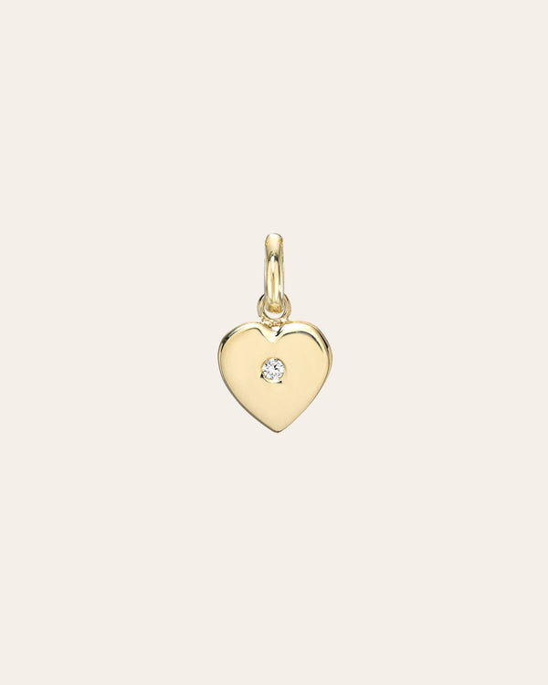 Gold heart-shaped pendant with a diamond on a light beige background